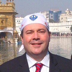 On Kenney’s head is a Sikh head scarf, also known as a rumal, which is usually worn by non-Sikh visitors to the Sikh Gurdwaras.